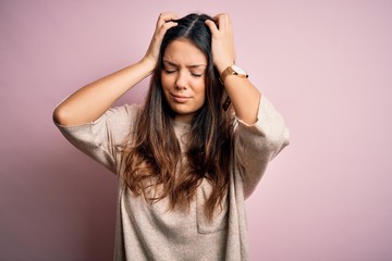 Young beautiful brunette woman wearing casual sweater standing over pink background suffering from...