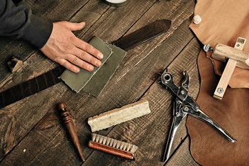 Working process of the leather belt in the leather workshop. Man holding tool. Tanner in old tannery. Wooden table background. Close up man arm. Maintenance concept. Goods production.