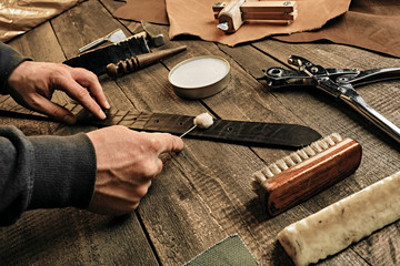 Working process of the leather belt in the leather workshop. Man holding tool. Tanner in old tannery. Wooden table background. Close up man arm. Maintenance concept. Goods production.
