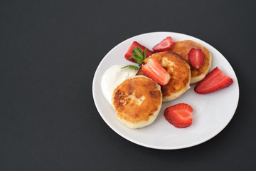 Russian and Ukrainian cuisine. Breakfast. Cottage cheese pancakes. Cheesecakes with fresh strawberries, mint and sour cream sauce in a white plate on a light grey background. Copy space mocap top view