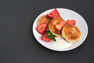 Russian and Ukrainian cuisine. Breakfast. Cottage cheese pancakes. Cheesecakes with fresh strawberries, mint and sour cream sauce in a white plate on a light grey background. Copy space mocap top view