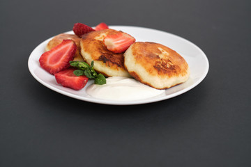 Russian and Ukrainian cuisine. Breakfast. Cottage cheese pancakes. Cheesecakes with fresh strawberries, mint and sour cream sauce in a white plate on a light grey background. Copy space mocap close-up