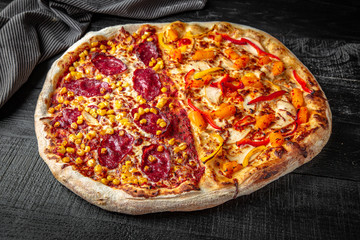Tasty hot italian big two-in-one pizza  with chicken, pineapple and pepperoni and corn on black wooden table. Pizzeria menu. Concept poster for Restaurants or pizzerias