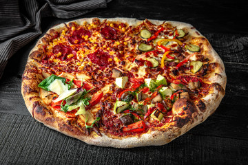 Tasty hot large double italian pizza with vegetable and meat on black wooden table. Pizzeria menu. Concept poster for Restaurants or pizzerias
