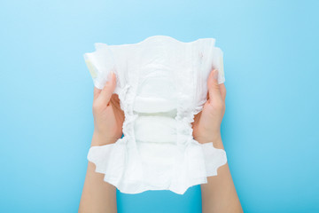 Young mother hands holding opened white baby diaper on light blue table background. Pastel color....