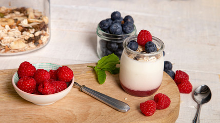 Closed shot of glass jar of white yogurt with fresh raspberry and blueberry on serving board on rustic table,