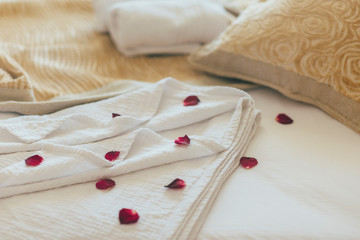 Luxury wellness and spa hotel room arranged for romantic weekend. Honeymoon suite bedroom decorated with rose petals on bed sheets.