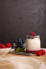 .Breakfast with white yogurt with fresh raspberries and blueberries on the serving board on the rustic table. Vertical image