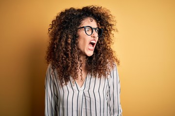 Young beautiful woman with curly hair and piercing wearing striped shirt and glasses angry and mad screaming frustrated and furious, shouting with anger. Rage and aggressive concept. © Krakenimages.com