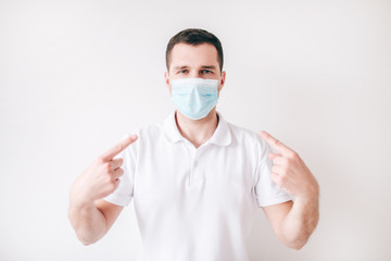 Young sick man isolated over white background. Guy wear facial medical mask and point on it with two fingers. Protection from virus and bacteria.