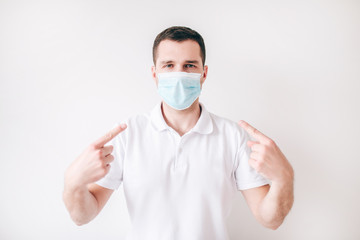 Young sick man isolated over white background. Guy wear facial medical mask and point on it with two fingers. Protection from virus and bacteria.