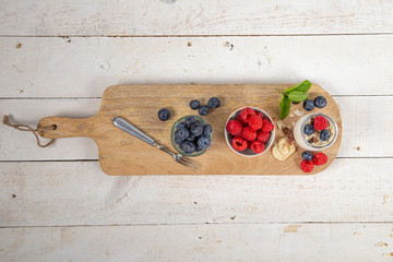 Aerial view of wooden cutting board with various forest berries and natural yogurt. Blueberries and raspberries.