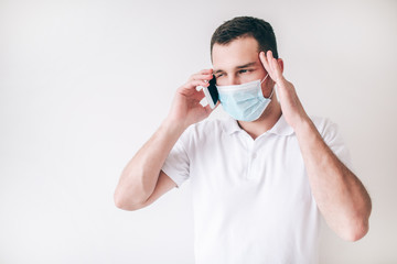 Young sick man isolated over white background. Guy wear facial medical protection mask. Calling doctor and adjusting medical appointment with doctor using smartphone.