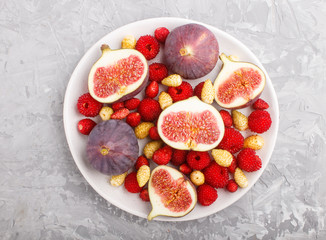 Fresh figs, strawberries and raspberries on white plate on gray concrete background. top view