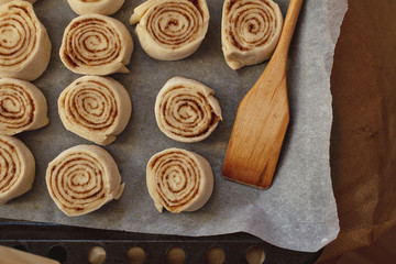 cooking home cinnabon buns from yeast dough on black aking sheet with baking paper anda wooden spatula