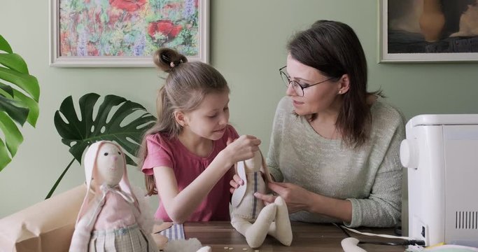 Mother and daughter child together sewing toy hare doll, hobbies and leisure at home