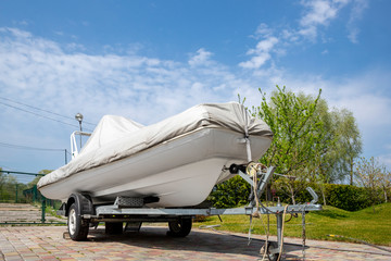 Big modern inflatable motorboat ship covered with grey or white protection tarp standing on steel...