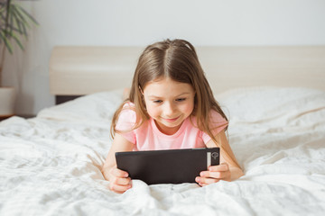 Happy teen girl watching online movie stream with digital mobile tablet and lying on bed at home in morning, video call connection, social distancing, network technology concept