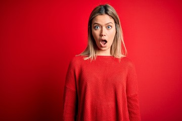 Young beautiful blonde woman wearing casual sweater over red isolated background afraid and shocked...