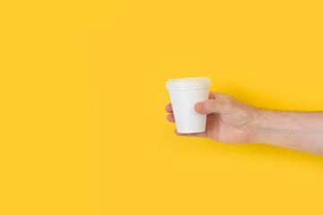 Mano de hombre sosteniendo una vaso descartable de café sobre fondo amarillo brillante aislado. Vista de frente. Copy space