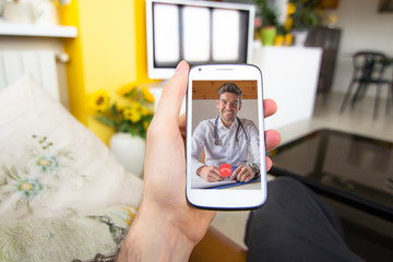 Young man holding smartphone making video call with doctor at home