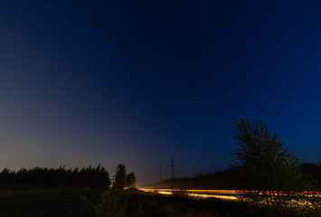 Sunset and starry sky over the forest. Lights of passing cars on the road.