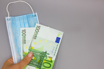 Close-up of medical or surgical blue color mask in the hand of a young woman on a gray background. The concept of medical supplies or accessories for personal protection.  Space for text. Mock up.
