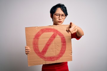 Young beautiful asian girl holding banner with prohibited signal over white background pointing...