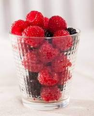 handful of fresh raspberry and blackberry berries in glass on white background