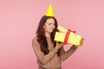 Portrait of curious happy woman with party cone on head looking inside box, unpacking gift and smiling pleased, satisfied with present, celebrating birthday, anniversary. indoor studio shot isolated