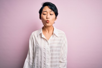 Young beautiful asian girl wearing casual shirt standing over isolated pink background making fish face with lips, crazy and comical gesture. Funny expression.