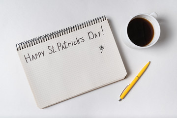 Notebook with words HAPPY St PATRICKS DAY. Coffee and pen. Top view, white background