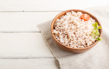 Unpolished rice porridge in wooden bowl on a white wooden background. side view, copy space.