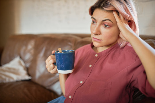 Sad Young Housewife With Depressed Look Having Rest On Sofa, Drinking Stress Relief Herbal Tea, Tired Of Cleaning House, Noisy Children Because Family Has To Stay At Home During Oquarantine