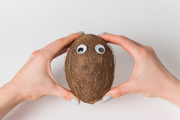 Female hands holding brown coconut on white background. coconut with Googly eyes