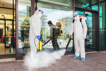 Professional workers in hazmat suits disinfecting outdoor of mall, pandemic health risk, coronavirus