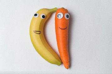 Banana and carrot with the Googly eyes and smiles on white background. Vegetarians concept