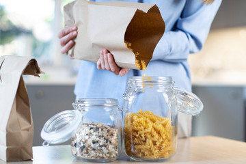 Close Up Of Woman Pouring Pasta From Plastic Free Packaging Paper Bag Into Storage Jar