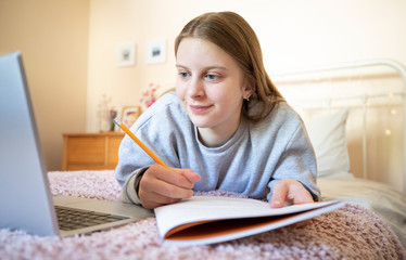 Teenage Girl Lying On Bed In Bedroom With Laptop Studying And Home Schooling