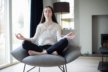 Peaceful Teenage Girl Meditating Sitting In Chair At Home