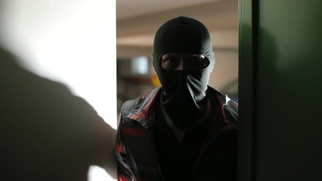 The formation of the composition of the attack. A man in a mask on his face comes into the door of the room. 