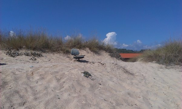 Low Angle View Of Chair On Sandy Beach Against Blue Sky