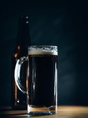 A mug of dark beer ale and a beer bottle on the table