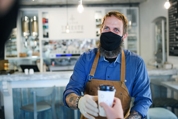 Fototapeta na wymiar Man with face mask serving customer, shop open after lockdown quarantine.