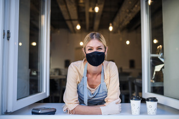 Woman with face mask serving coffee through window, shop open after lockdown.