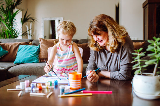 Grandmother and granddaughter drawing together with watercolors at home. Little girl has a lesson with her drawing teacher.