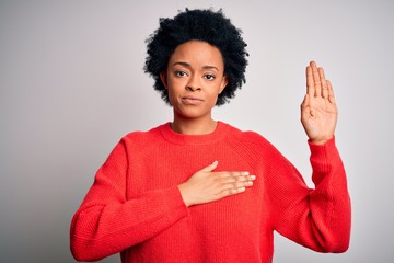 Young beautiful African American afro woman with curly hair wearing red casual sweater Swearing with hand on chest and open palm, making a loyalty promise oath
