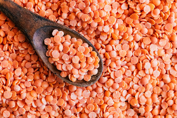 Lentilles rouges corail dans une cuillère en bois et arrière plan lentilles