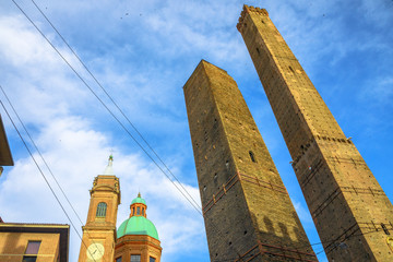 Perspective bottom view of Two Towers of Bologna, symbol of city in blue sky, Italy. Asinelli tower and Garisenda tower in historic downtown with clock tower of city.