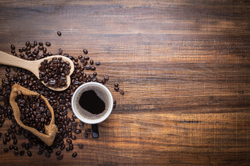 Black and brown coffee beans with cup of hot drink on  wooden table, top view copy space